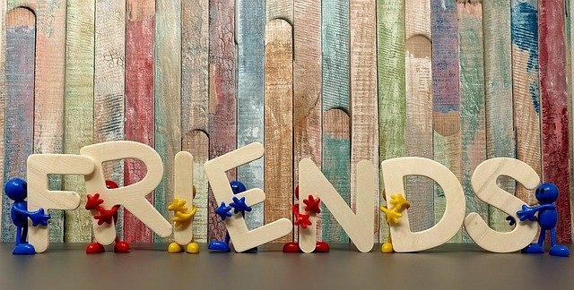 This is a picture of a multicoloured wooden slatted wall.  In front of it is the word Friends. The letters of the word are held up by cartoon figures. The purpose of the picture is to symbolise Friendship