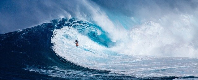 A vivid blue picture of a breaking wave in the ocean.  There is a small figure of a water surfer, surfing the wave.  The picture represents joy, happiness and a good feeling.  It's aim is to encourage us to focus on the good.