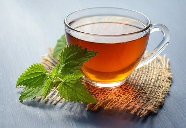 This is a picture of a clear glass tea cup sat on a hessian fabric. In the cup is a light brown liquid possibly tea. Next two the cup is a sprig of mint. The picture is meant to invoke a relaxed feeling the sort of feeling you get from beauty therapy.