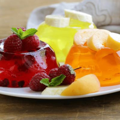 A picture of a white plate with three jelly cakes on it. One is a red jelly raspberry flavour with some raspberries on top of it as well as some lying next to it. The raspberries are garnished with mint. There is an orange jelly with apple slices on top of it and a yellow jelly with banana slices on top of it. The purpose of the picture is to comment on mindset.