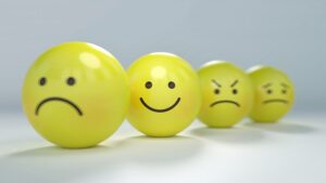 Four yellow emoji balls three have negative emotions depicted. They are slightly hazy in appearance. The fourth has a clear smiley face. The purpose of this picture is encourage people to choose happiness.