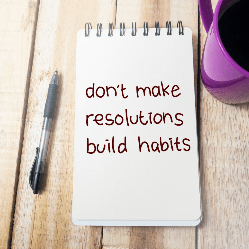 A picture of a note pad on a wooden back ground . On the note pad it says "Don't make resolutions build habits". Next to the note pad on one side is a black pen and on the right hand side is a purple cup filled with coffee. The purpose of the picture is to emphasis the importance of habits and habit"