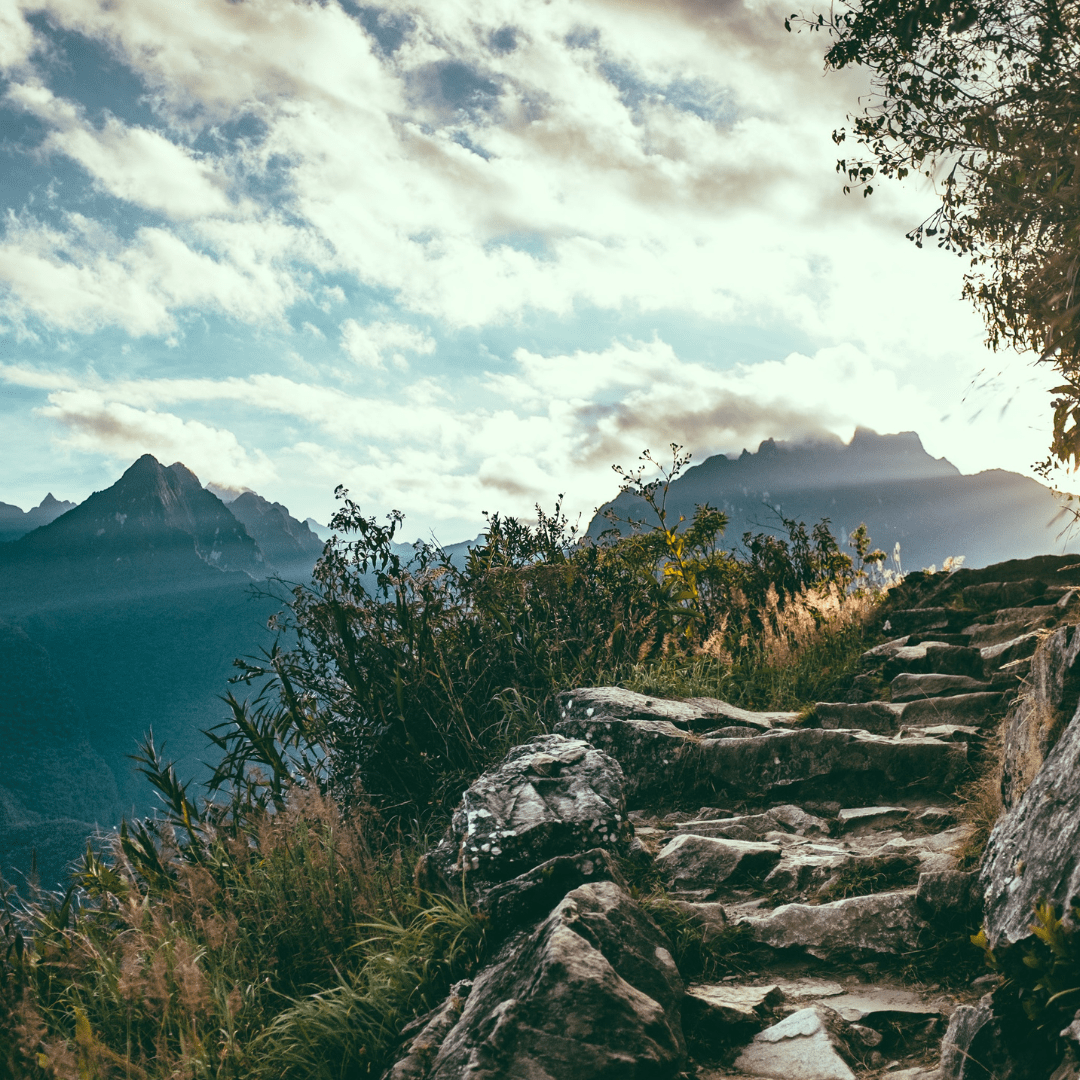 This is a colourful picture of a mountain landscape. The colours are the natural colours of nature. Blues, green, stone, white, sunshine. In the background are mountains in the foreground, on the right of the picture are some stone steps heading upwards. The stone steps appear as if they are high up on a mountain already. The purpose of this picture is to suggest the benefits of following a well trodden path and having faith.   