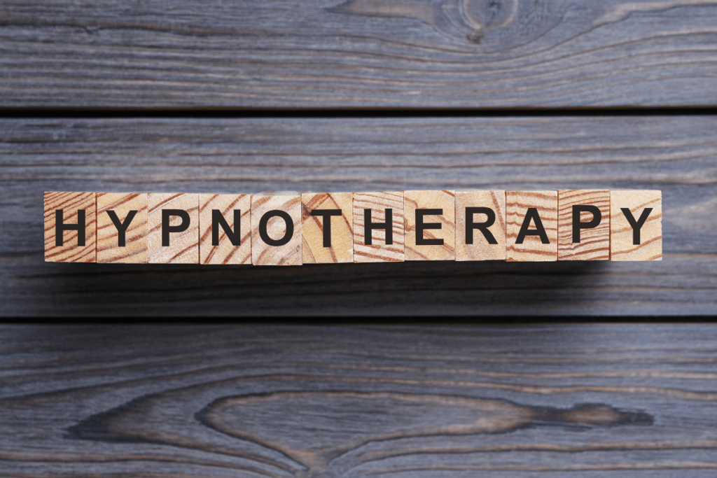 The picture is of three horizontal black boards of wood that are slotted together. On the boards is are light blocks of wood with black letters on it. The letters spell Hypnotherapy. The letters have the appearance of scrabble tiles. The purpose of the picture is to introduce a tool for hypnotherapy, i.e. a presentation around solution focused hypnotherapy. It helps clients achieve a Healthier mind