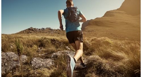 This is a picture of a hill runner running along a path towards a hill. There is a blue sky and the terrain is brown grass and rocks. The runner is wearing a light blue T-shirt, brown shorts and a small back pack. The poicture represents Resilience and how Hypnotherapy Swindon can help develop resilience.