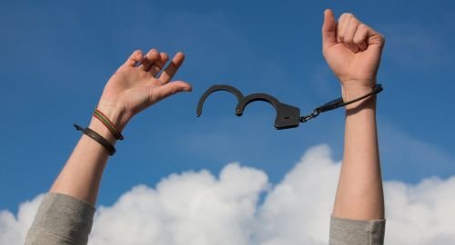 This a picture with a blue sky and cloud background. At the front of the picture are two arms with one arm having handcuffs attached to it the other is free of those handcuffs. The purpose of this picture is to indicate that clients can be free from OCD Obsessive compulsive disorder with the help of Hypnotherapy Swindon.