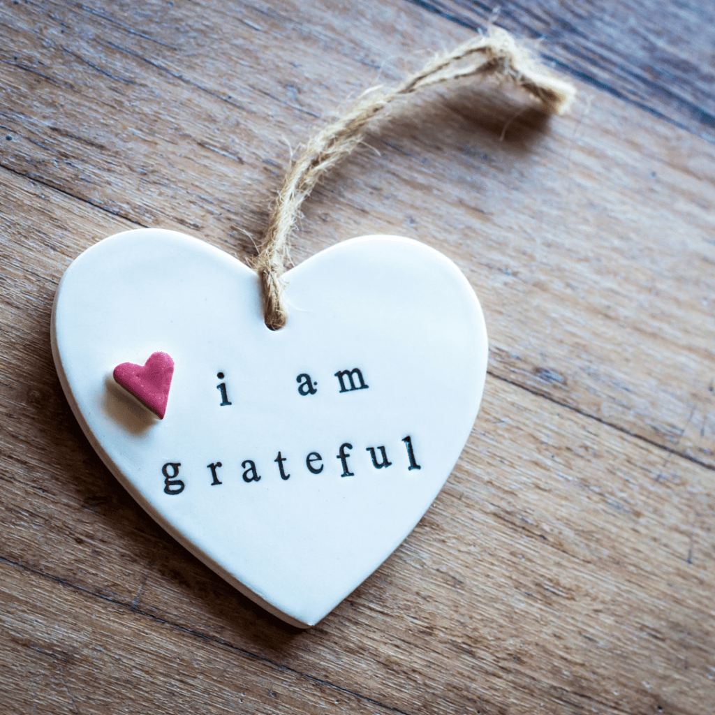 This a ceramic white heart shaped pendant with a frayed cord rope attached. On the pendent there is a small red heart and the words "I am Grateful" written on it. It emphasis the subject of the blog Gratitude. 